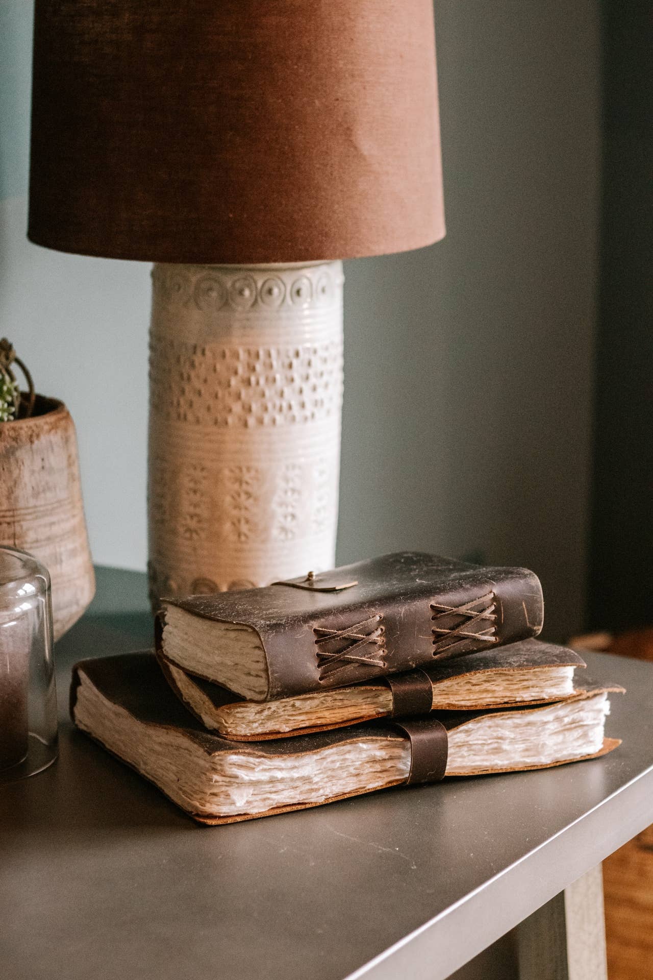 Stack of leather bound journals on a table with a lamp in the background