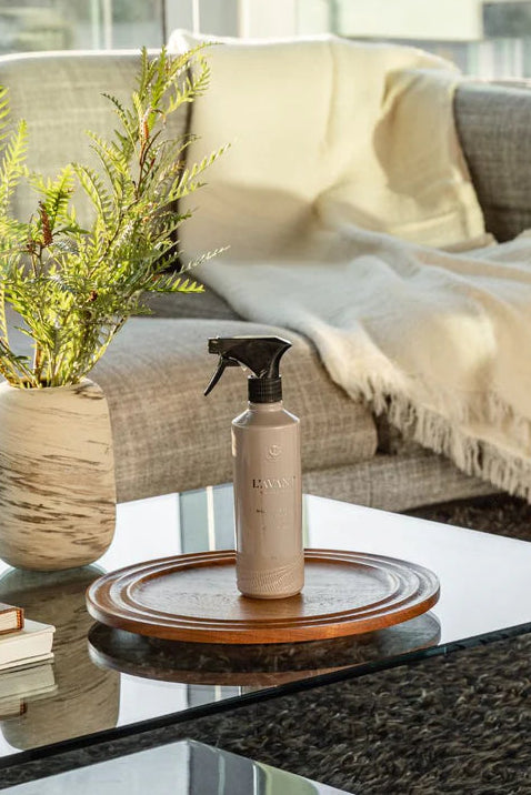Living room with a coffee table, plant, books, and a spray bottle. L'Avant Ambre Santal Multipurpose Cleaner