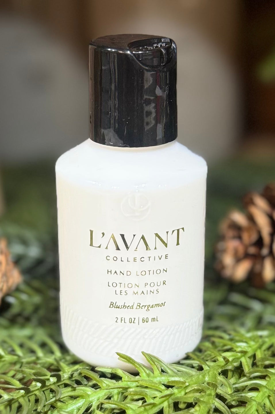 L'Avant Collective hand lotion bottle on a green background with pine cones.