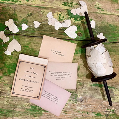 bOOKLET OF ENCOURAGING LOVE NOTES. Decorative setup with heart-shaped cutouts, a paper heart, and a small spool of thread on a wooden surface.