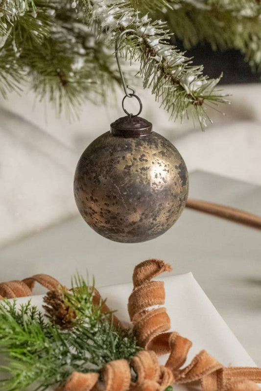 Decorative Christmas ornament hanging above wrapped presents with brown ribbon and greenery.