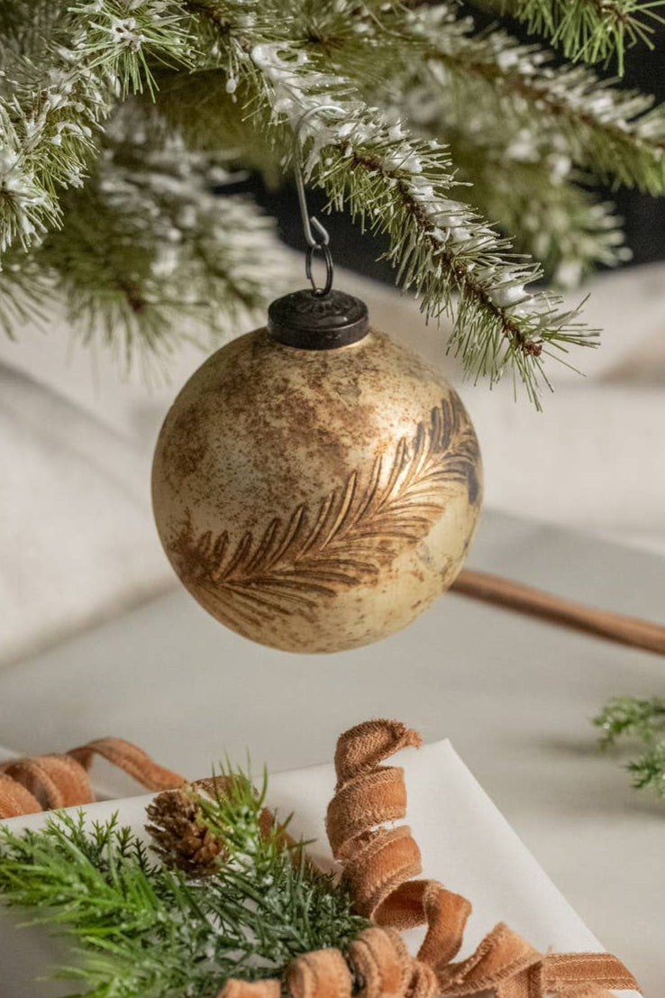 Decorative ornament hanging from a Christmas tree with a wrapped gift below.