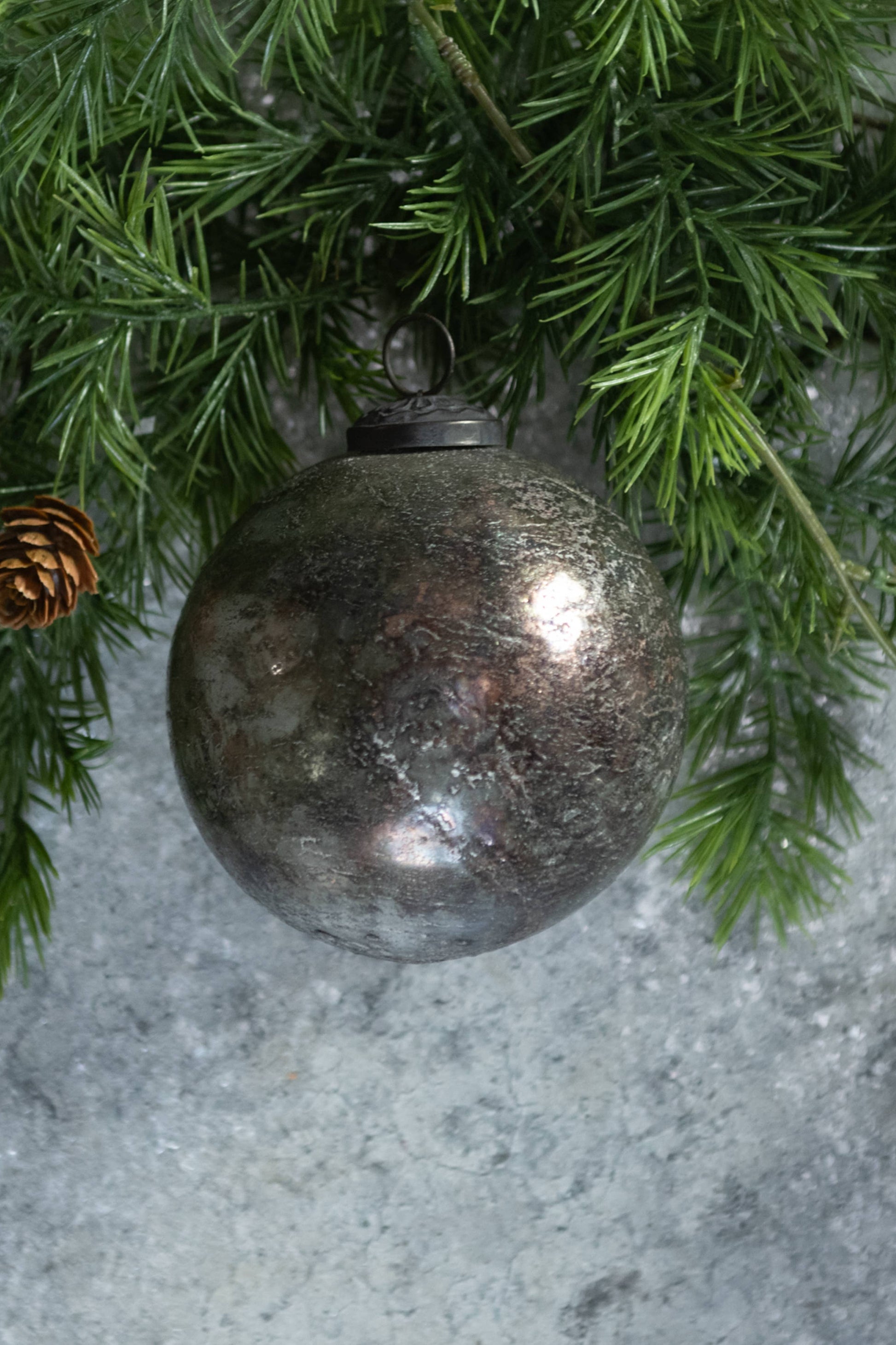 Decorative glass ball ornament on a branch with pine cones