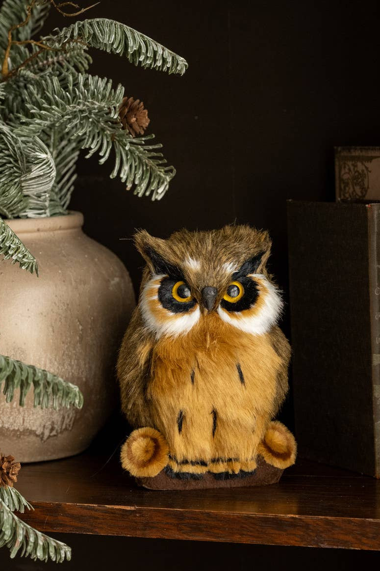 Stuffed owl toy on a wooden shelf with a vase and books in the background