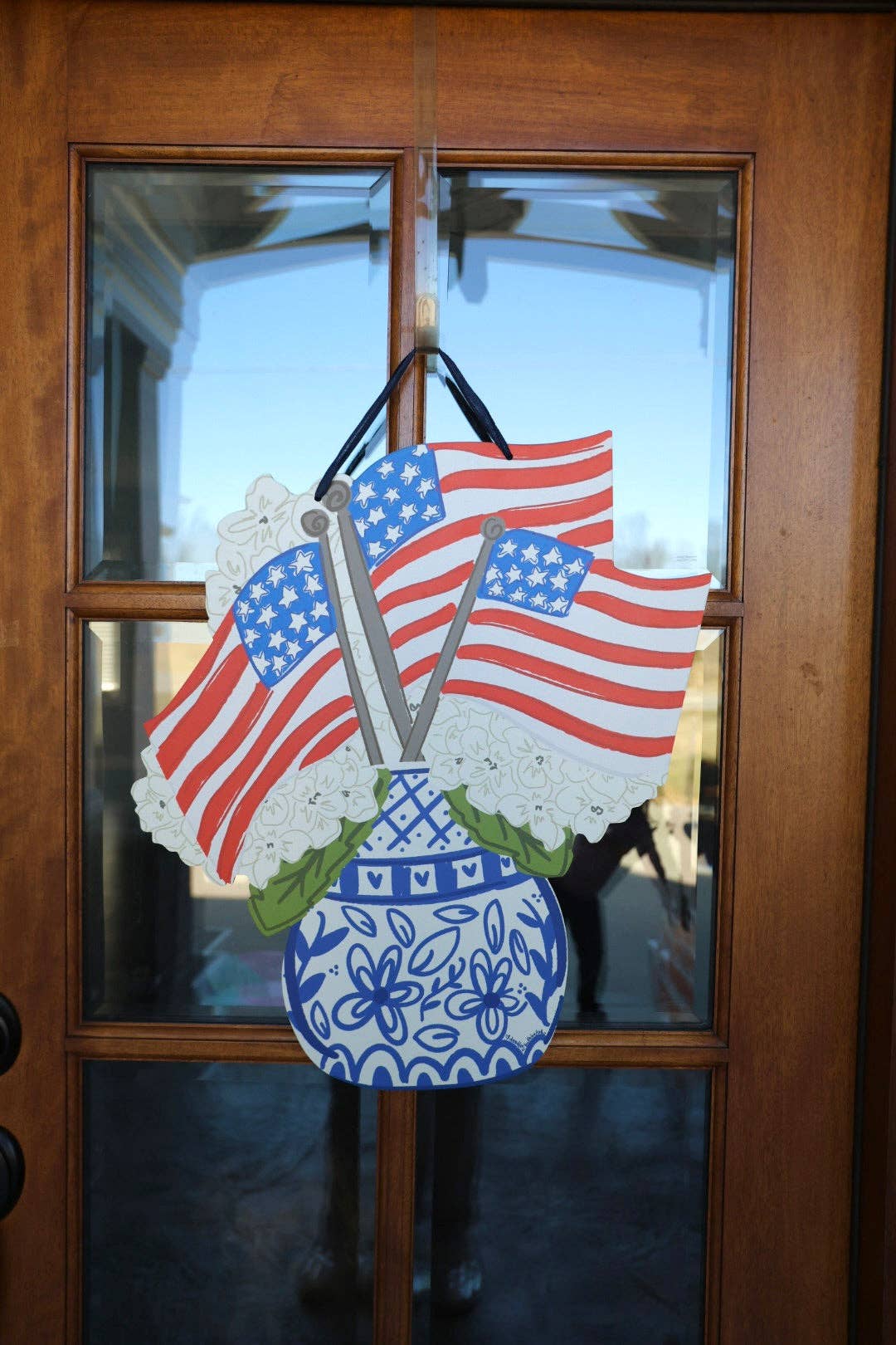Decorative door hanger with American flags and a blue vase on a wooden door.