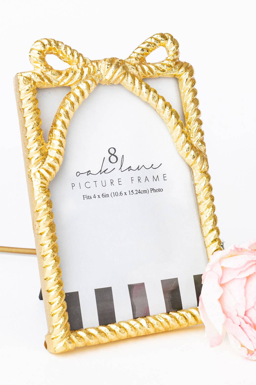 Gold picture frame with a decorative bow design on a white background with a pink rose.