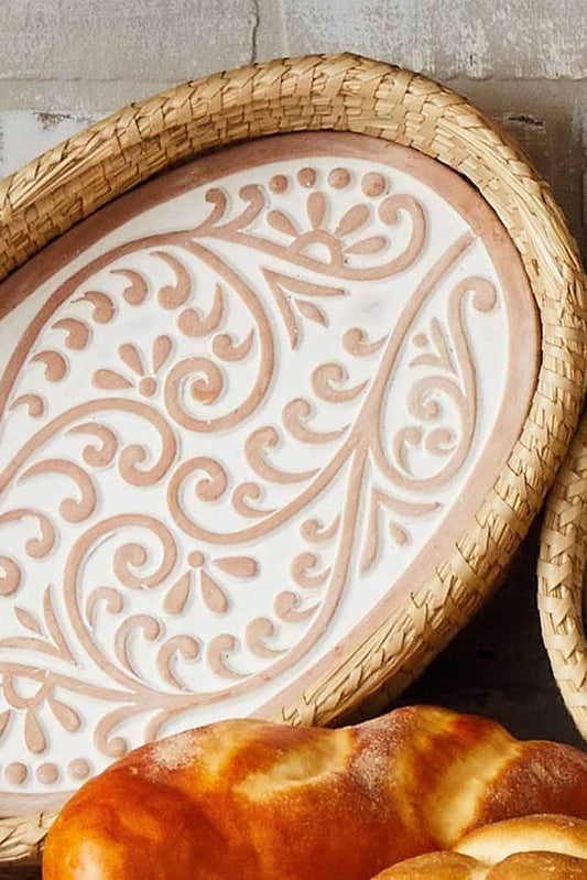 Decorative ceramic plate with intricate patterns on a woven tray, surrounded by bread.