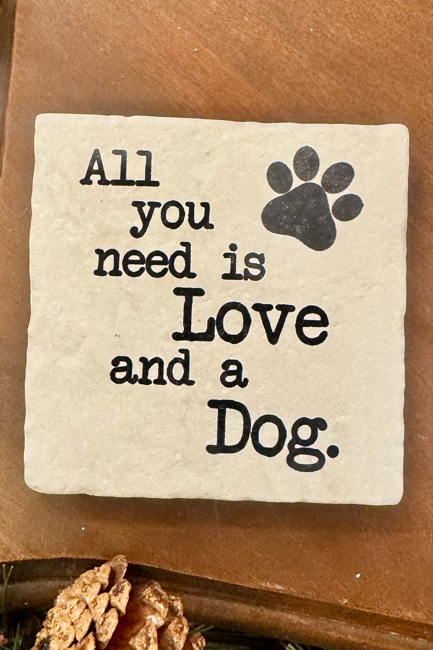Decorative stone with 'All you need is Love and a Dog' text and paw print on a wooden surface.