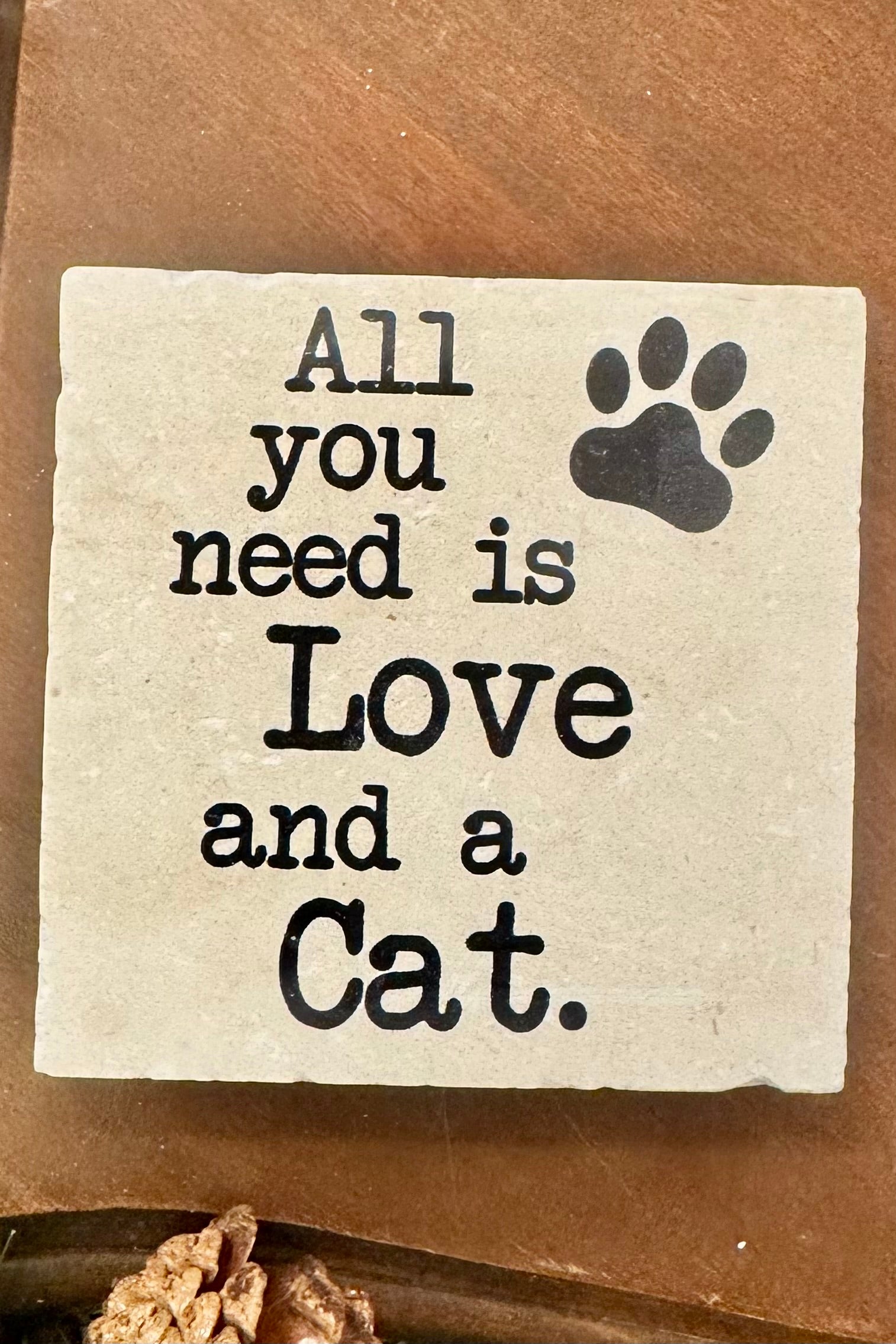 Square stone with 'All you need is Love and a Cat' text and paw print on a wooden surface.