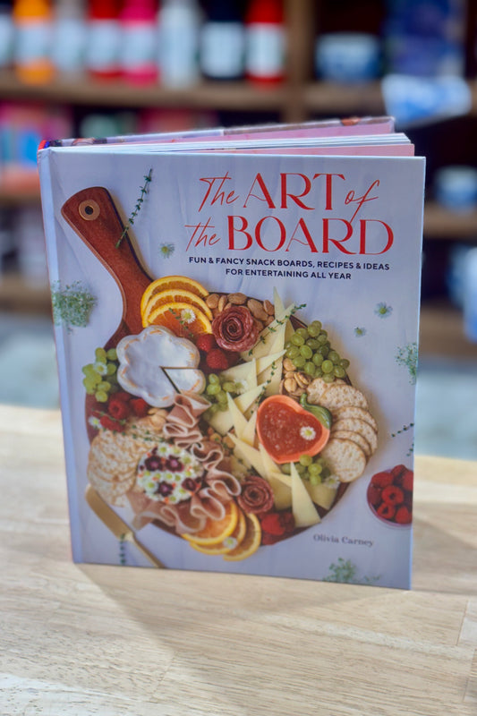 Book titled 'The Art of the Board' on a wooden surface with blurred shelves in the background