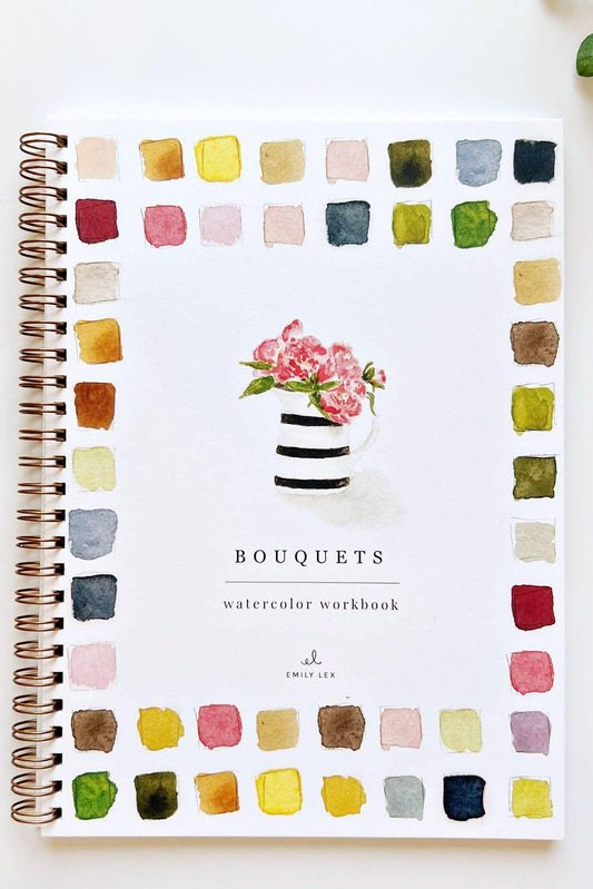 A spiral-bound watercolor workbook titled 'BOUQUETS' with a watercolor flower arrangement on the cover, surrounded by a border of painted color swatches. The workbook is photographed on a white surface with art supplies nearby, including a paint tube, paintbrush, and small plant.