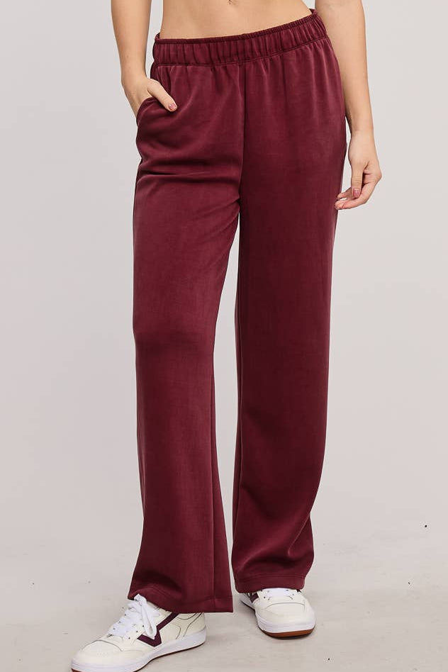 Woman wearing a white crop top and burgundy pants on a plain background