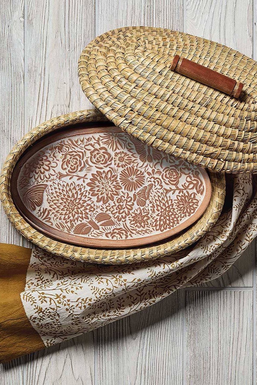 Woven basket with floral pattern, wooden lid, and wooden handle on a light wooden surface.