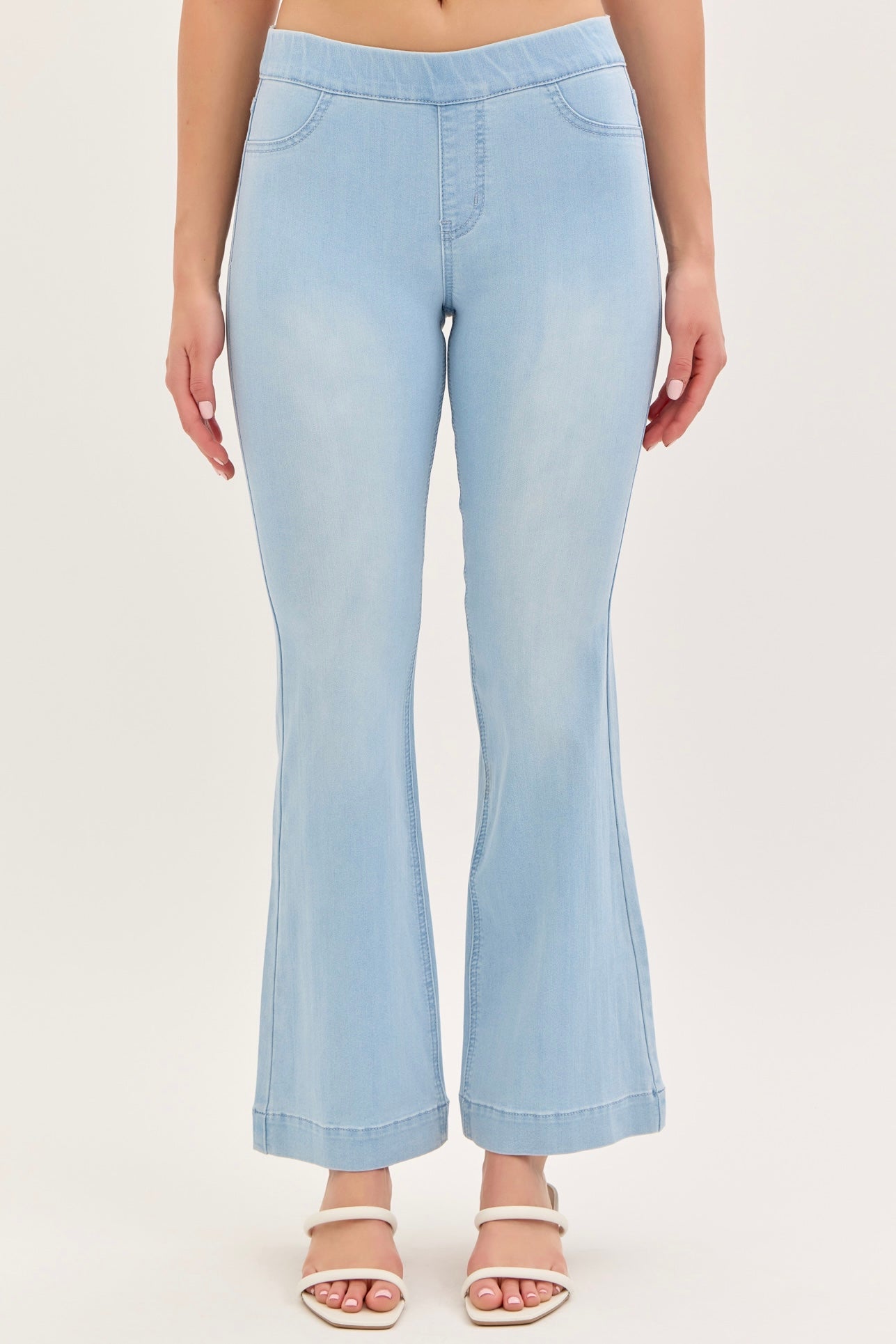 A pair of light wash flared denim jeggings with a mid-rise waist and a 30-inch inseam, featuring two front pockets and two back pockets. The model is wearing the jeggings and white sandals.