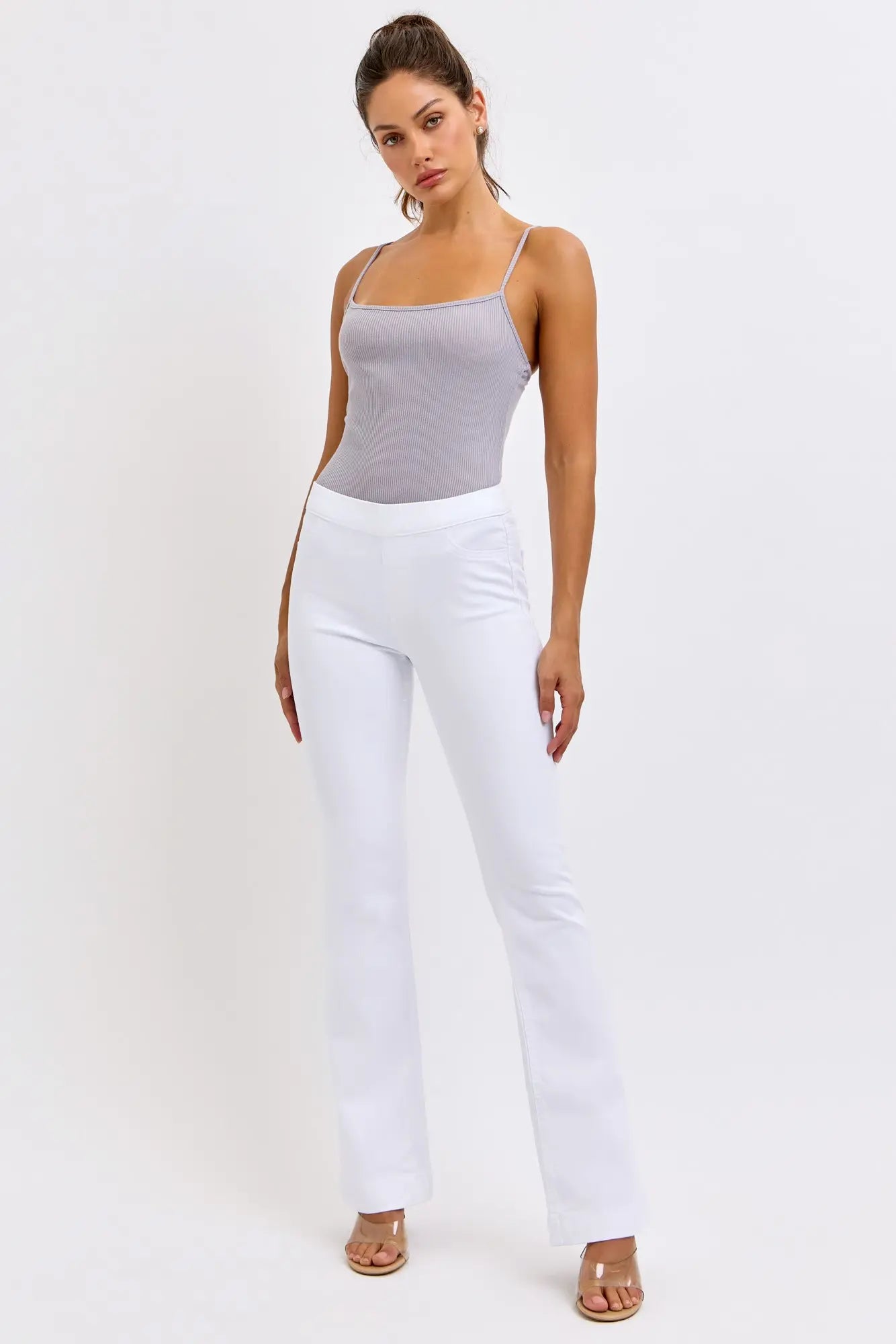 Woman wearing a gray tank top and white cello pants on a white background