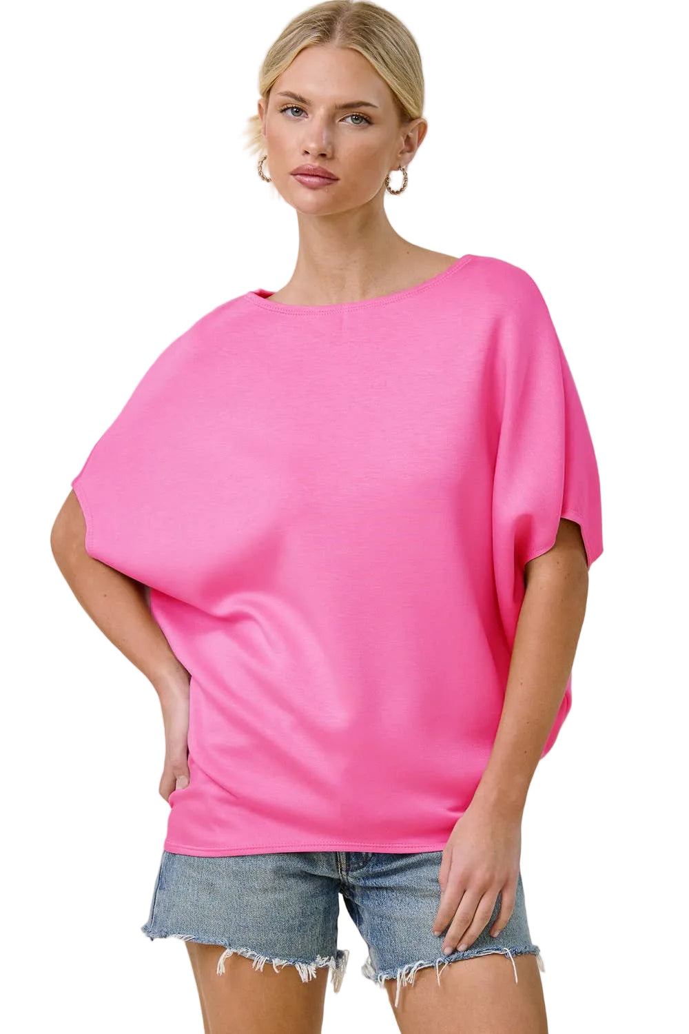 Woman wearing a bright pink top and denim shorts on a plain background