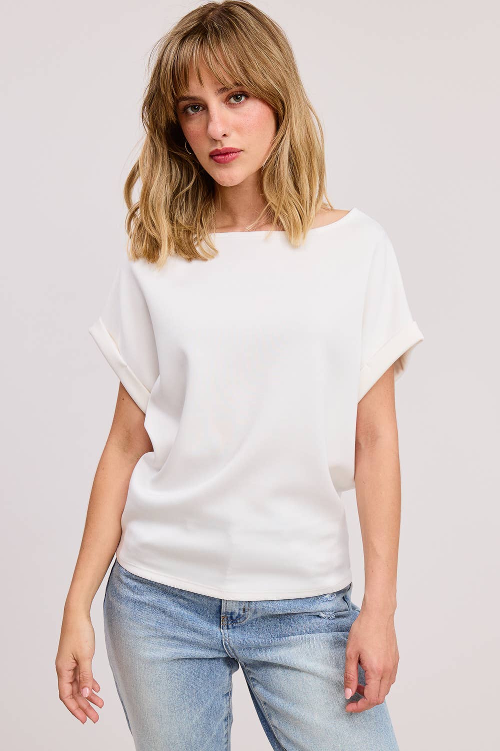 Woman wearing a white top and light blue jeans on a plain background