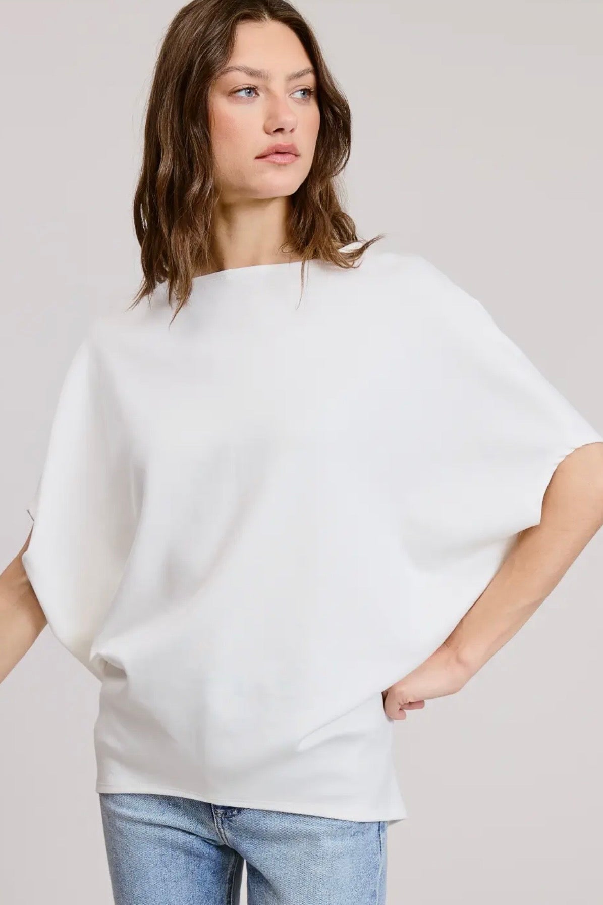 Woman wearing a white oversized sweater and blue jeans against a plain background