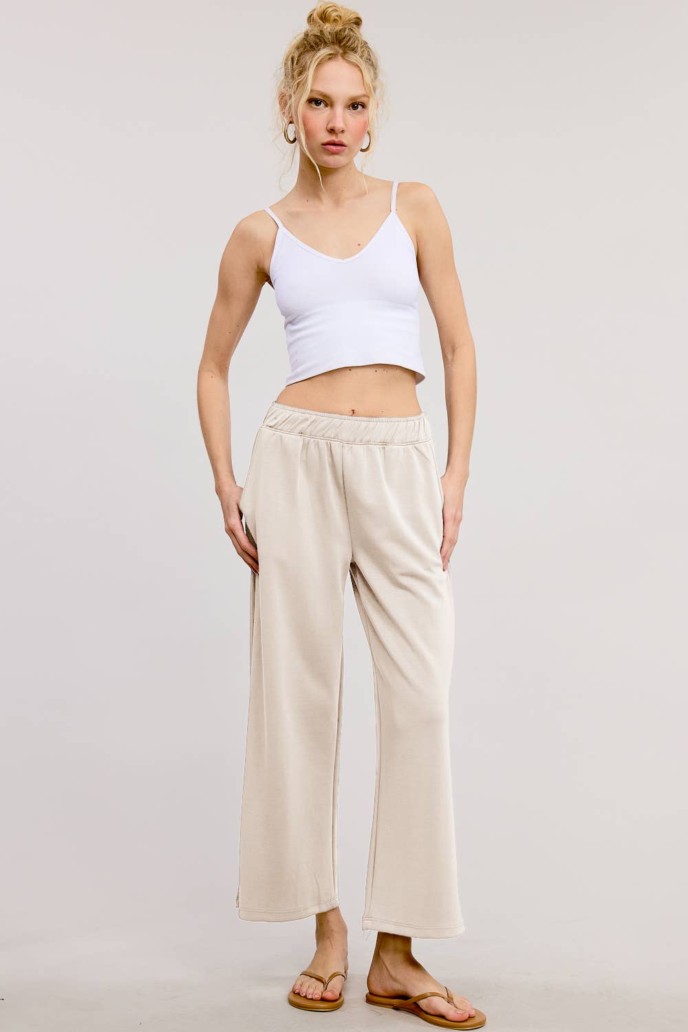 Woman wearing a white tank top and beige pants on a plain background