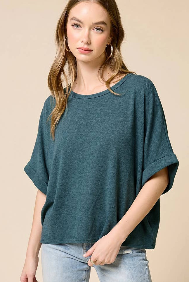 Woman wearing a teal oversized top and light blue jeans against a beige background