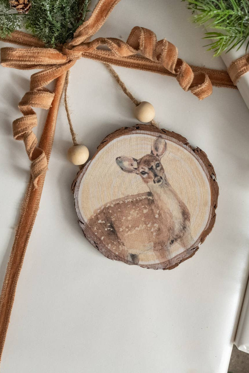 Wooden ornament with a deer design on a wrapped gift with brown ribbon and greenery.