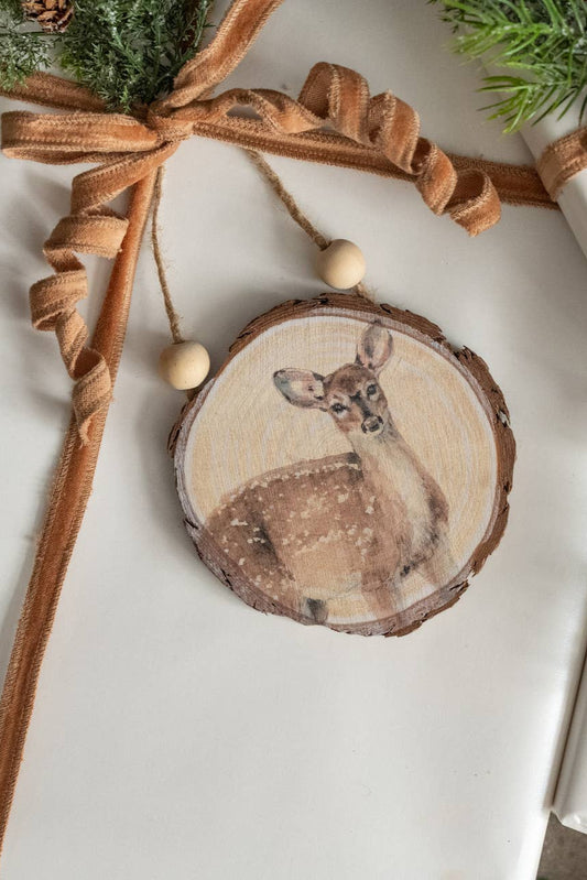 Wooden ornament with a deer design on a wrapped gift with brown ribbon and greenery.
