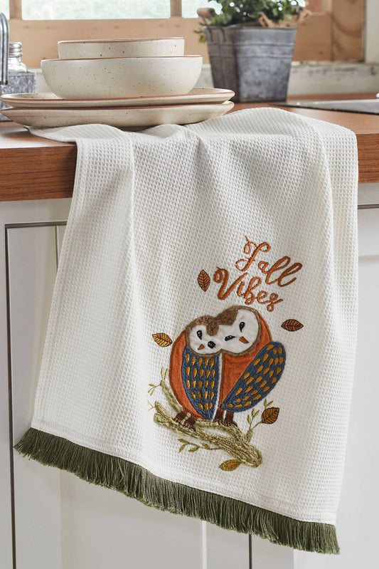 Kitchen towel with owl design and 'Fall Vibes' text hanging on a wooden cabinet.