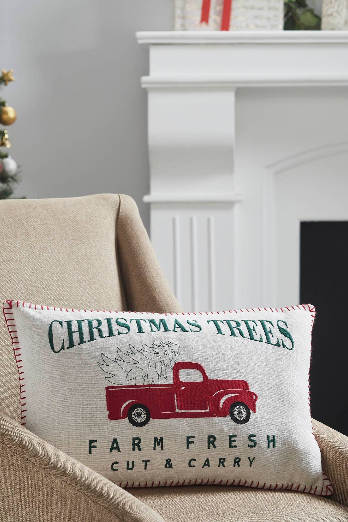 Decorative pillow with Christmas tree and truck design on a beige armchair in a festive setting.