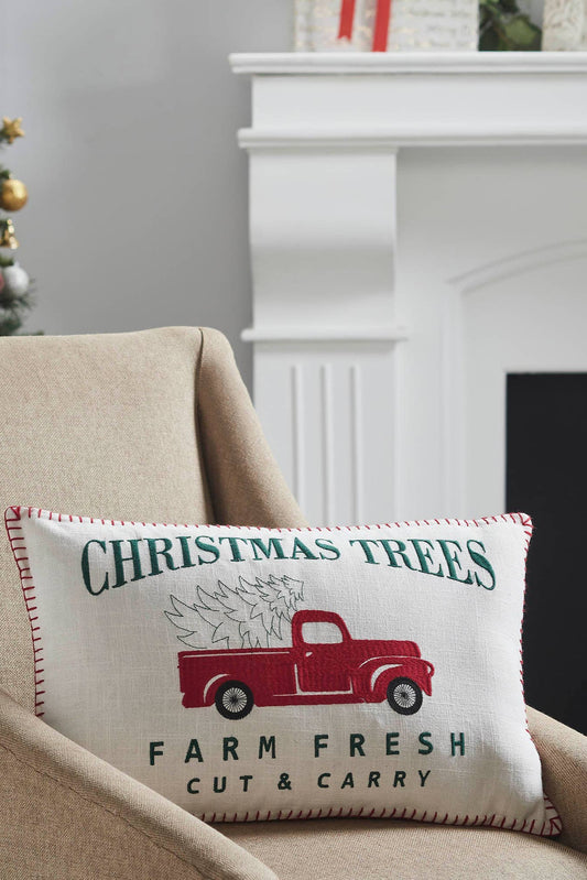 Decorative pillow with Christmas tree and truck design on a beige armchair in a festive setting.