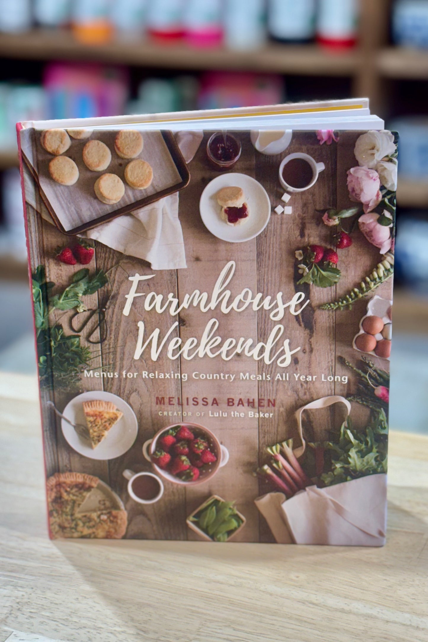 Cookbook titled 'Farmhouse Weekends' on a wooden surface with blurred background