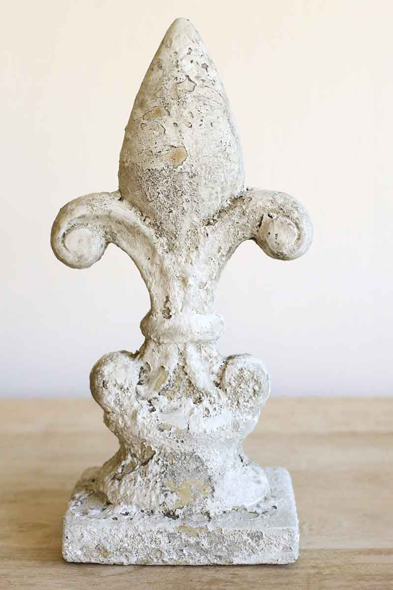 Decorative fleur-de-lis concrete sculpture on a wooden surface with a light background