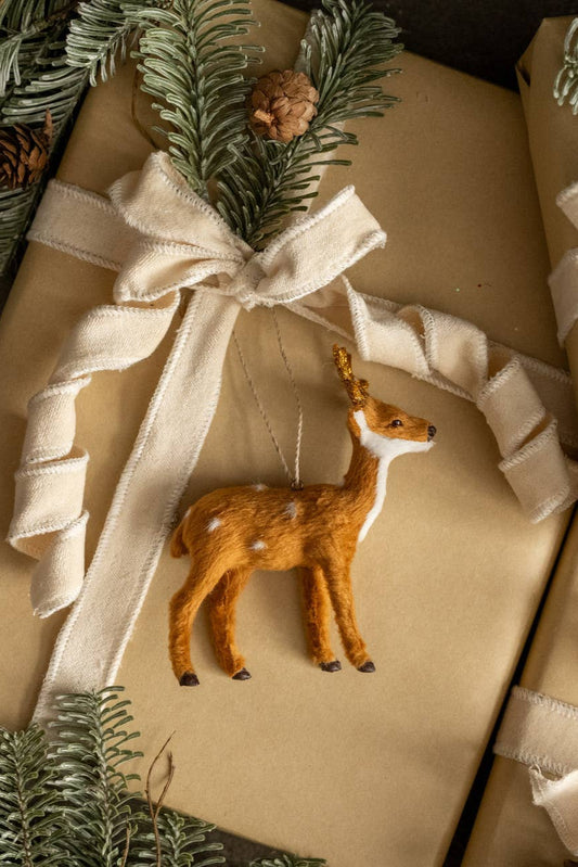 Gift wrapped in brown paper with a white ribbon and deer ornament, surrounded by greenery.