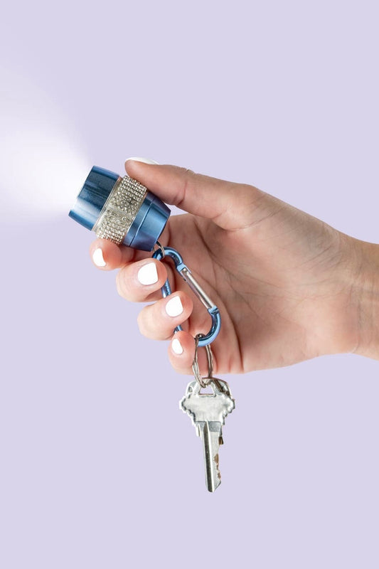 Hand holding a blue led flashlight keychain adorned with rhinestones  against a light purple background