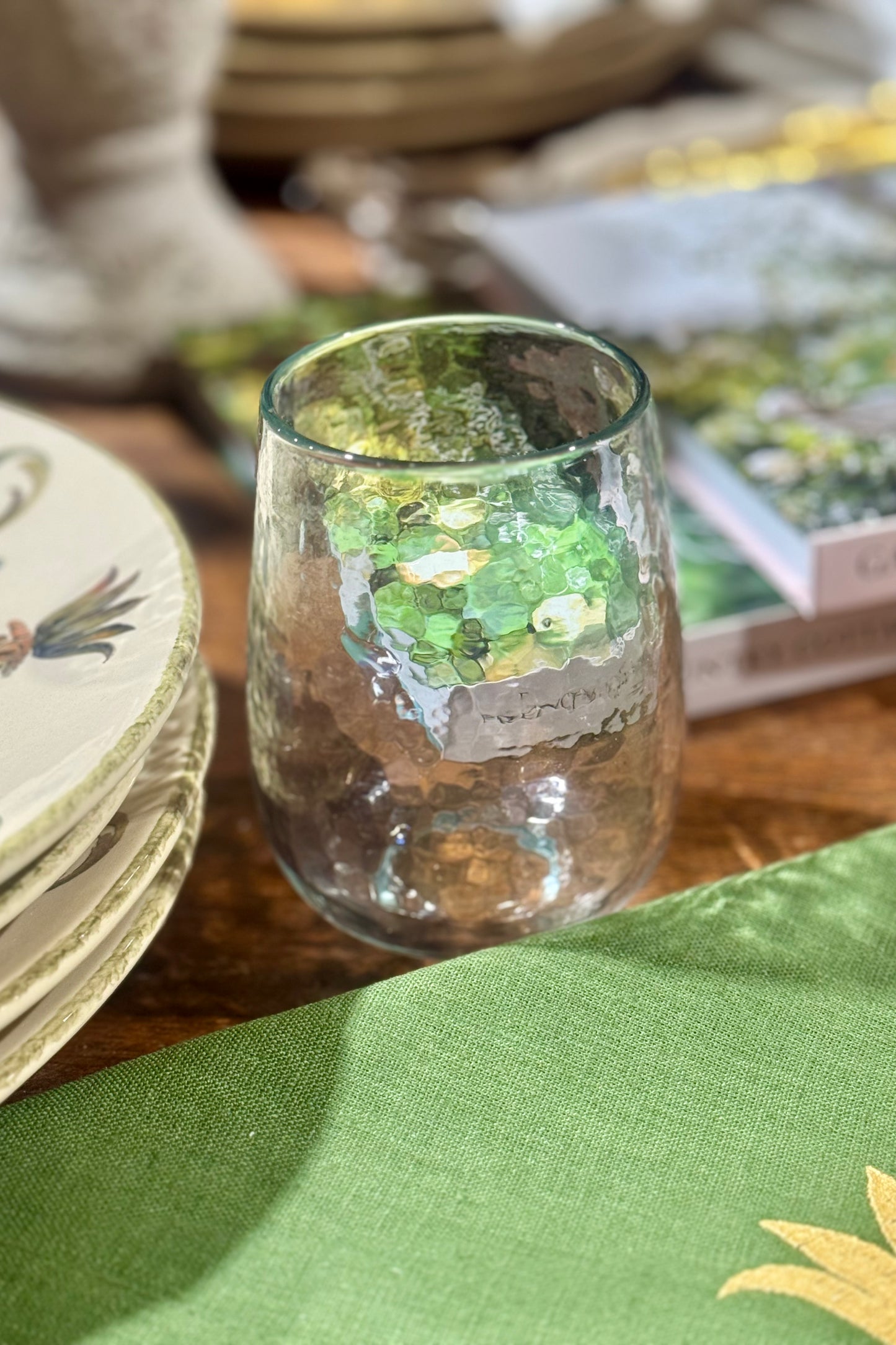 Hammered glass stemless wine glass on a table with a green napkin and blurred background