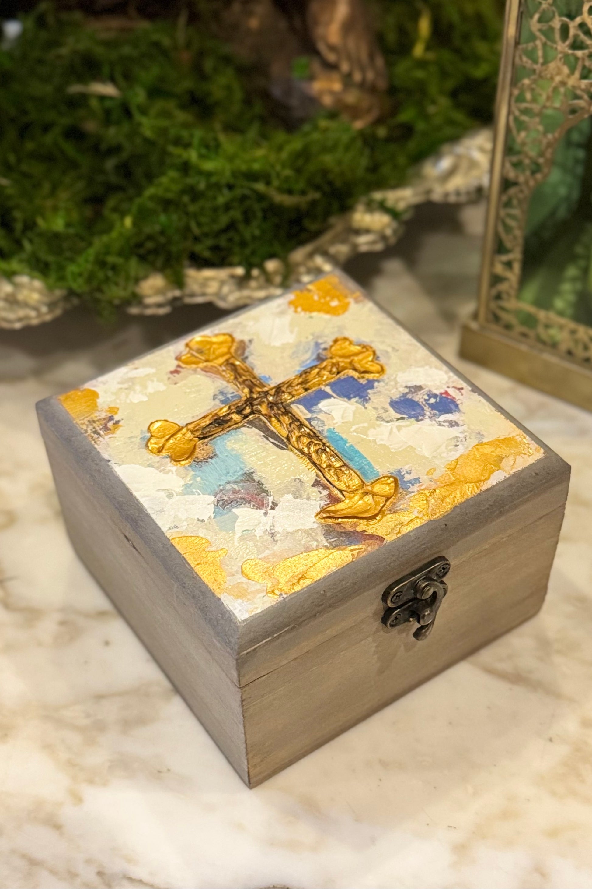 Wooden box with a decorative cross on top, placed on a marble surface.