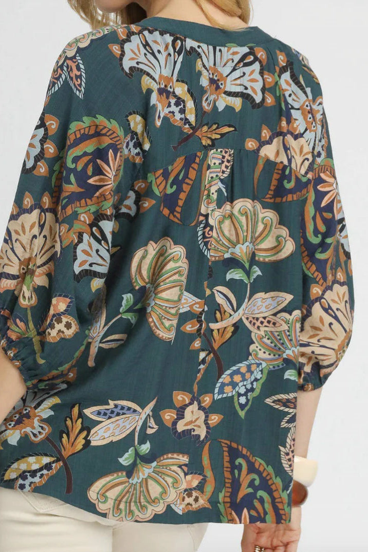 Teal floral patterned top worn by a person on a white background