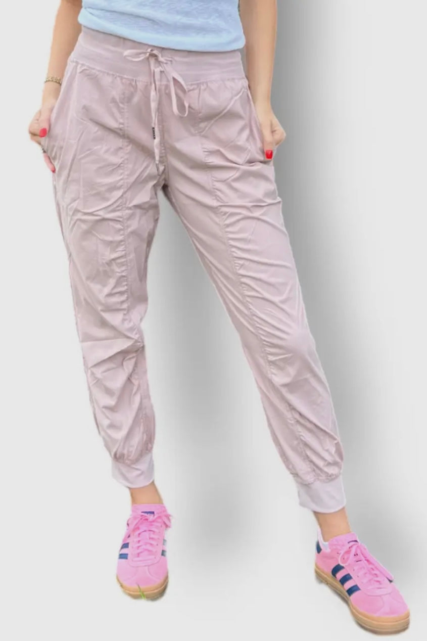 Person wearing light pink pants and pink sneakers on a plain background