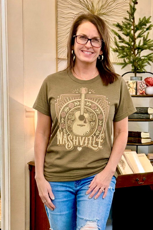 Woman wearing a green t-shirt with a guitar graphic and 'Nashville' text, standing indoors.