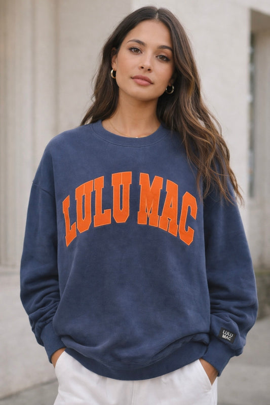 Woman wearing a navy blue sweatshirt with 'LULU MAC' in orange text, standing outdoors.