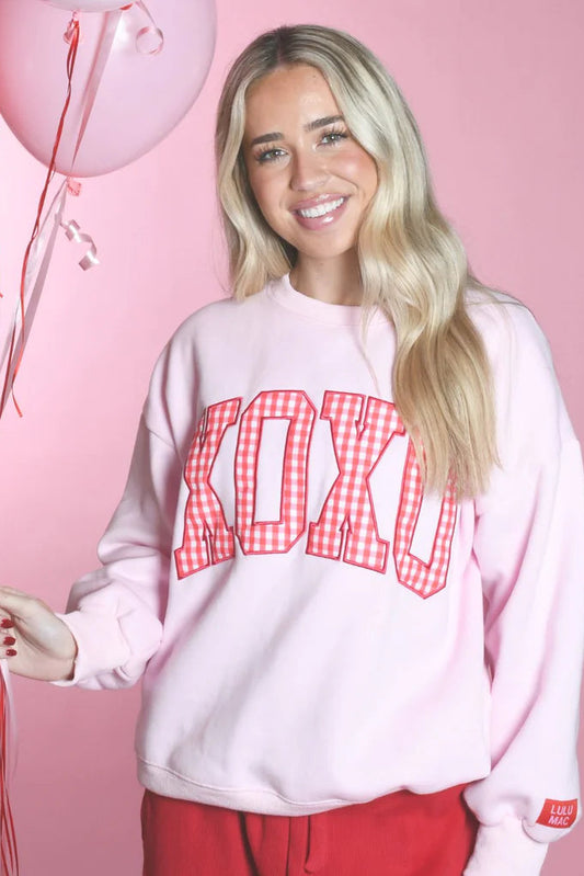 Person wearing a LULUMAC pink sweatshirt with XOXO print, holding balloons against a pink background