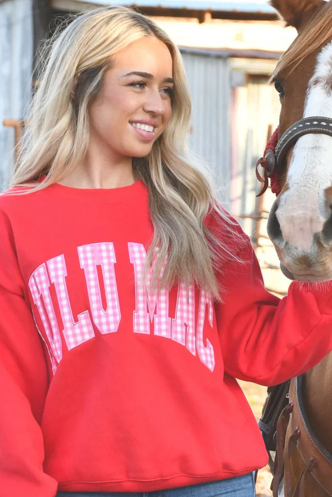 Woman in a red lulu mac sweatshirt petting a horse with a barn in the background