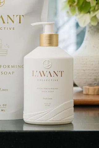 L'Avant dish soap bottle and container on a kitchen counter with a window and flowers in the background.