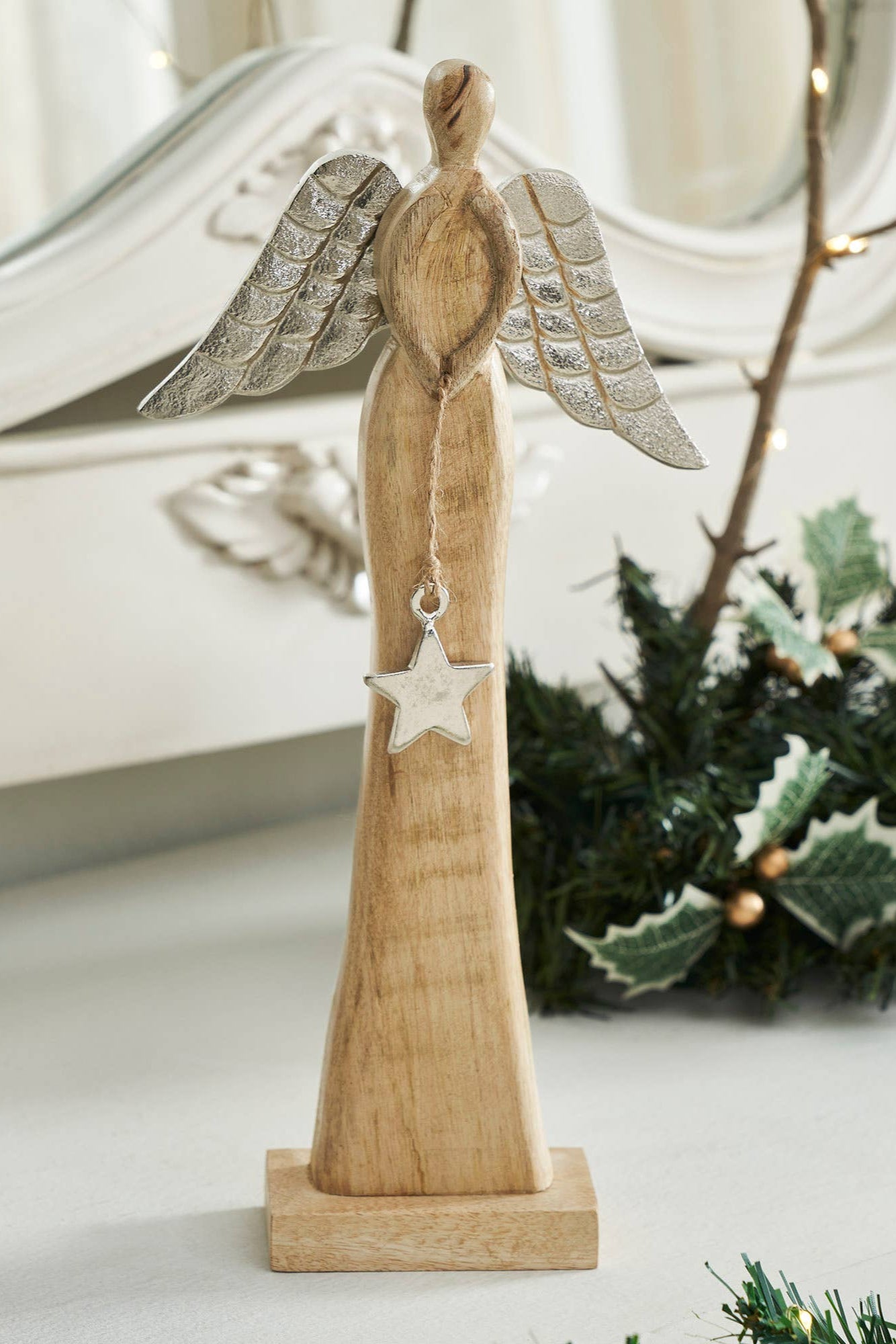 Wooden angel figurine with silver wings and star, placed on a surface with decorative elements.