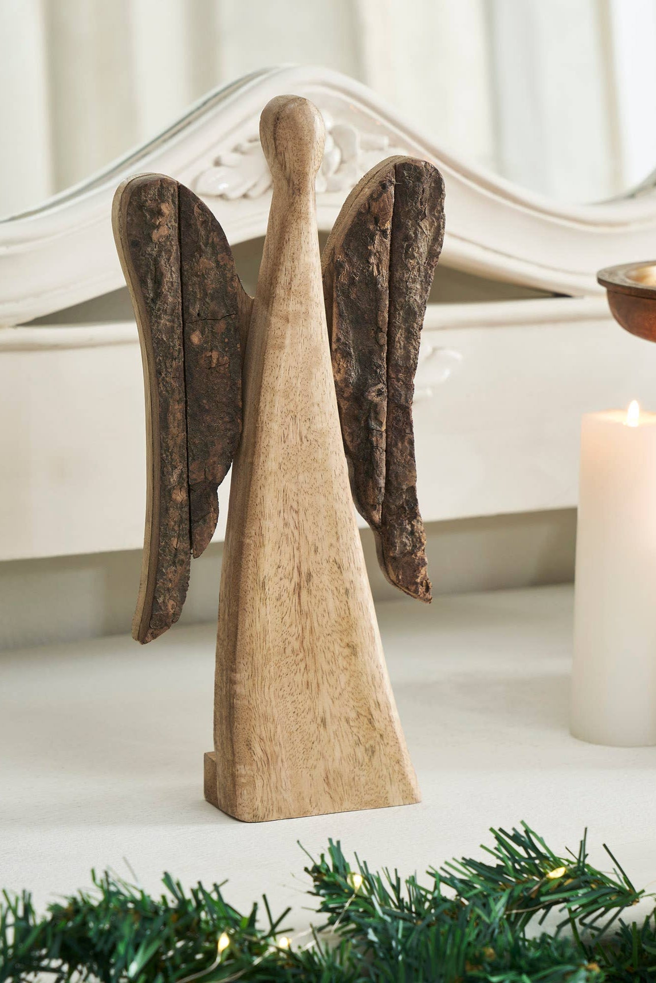 Wooden angel figurine on a decorative surface with candles and greenery