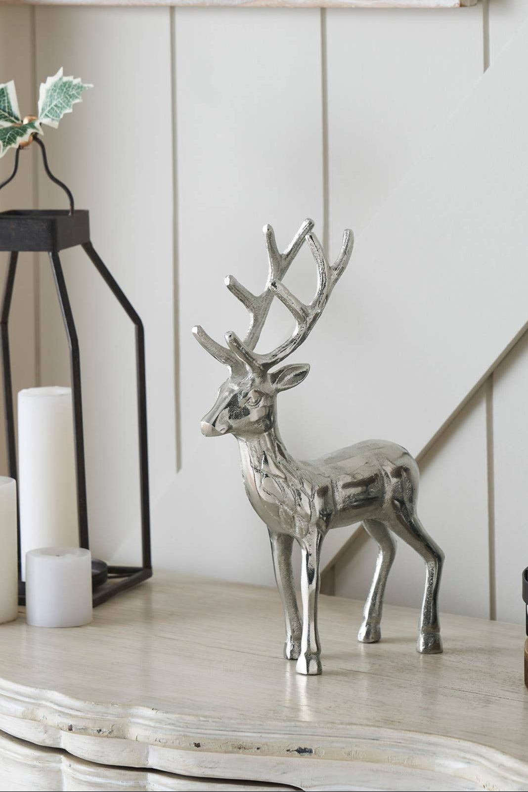 Decorative items including a silver deer, candles, and a lantern on a wooden surface.