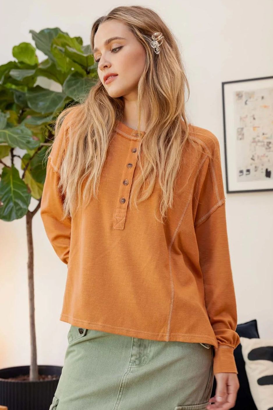 Woman wearing an orange long-sleeve top and green cargo pants in a living room setting.