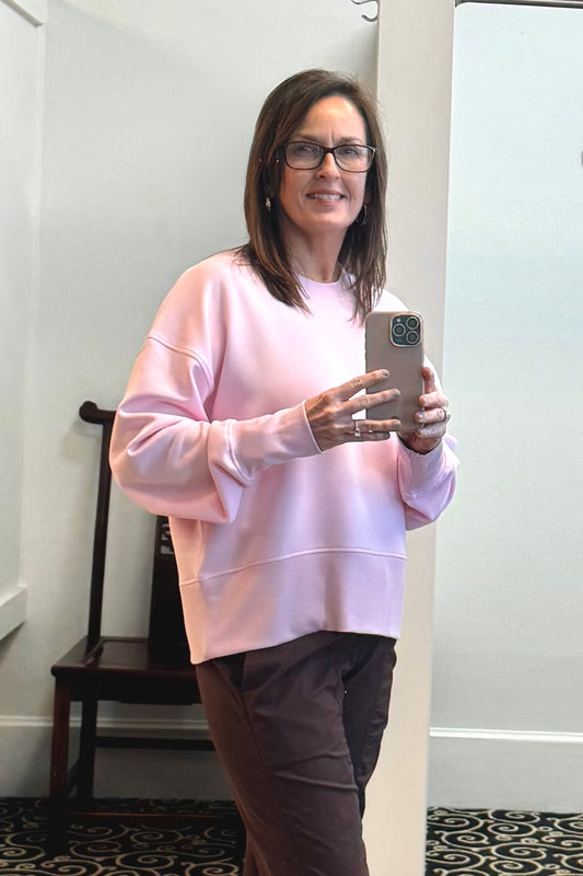 Woman taking a mirror selfie wearing a pink sweatshirt and glasses indoors.