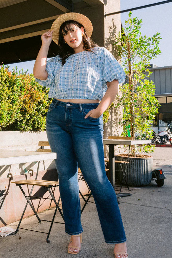 Woman wearing a blue patterned top and jeans standing outdoors.