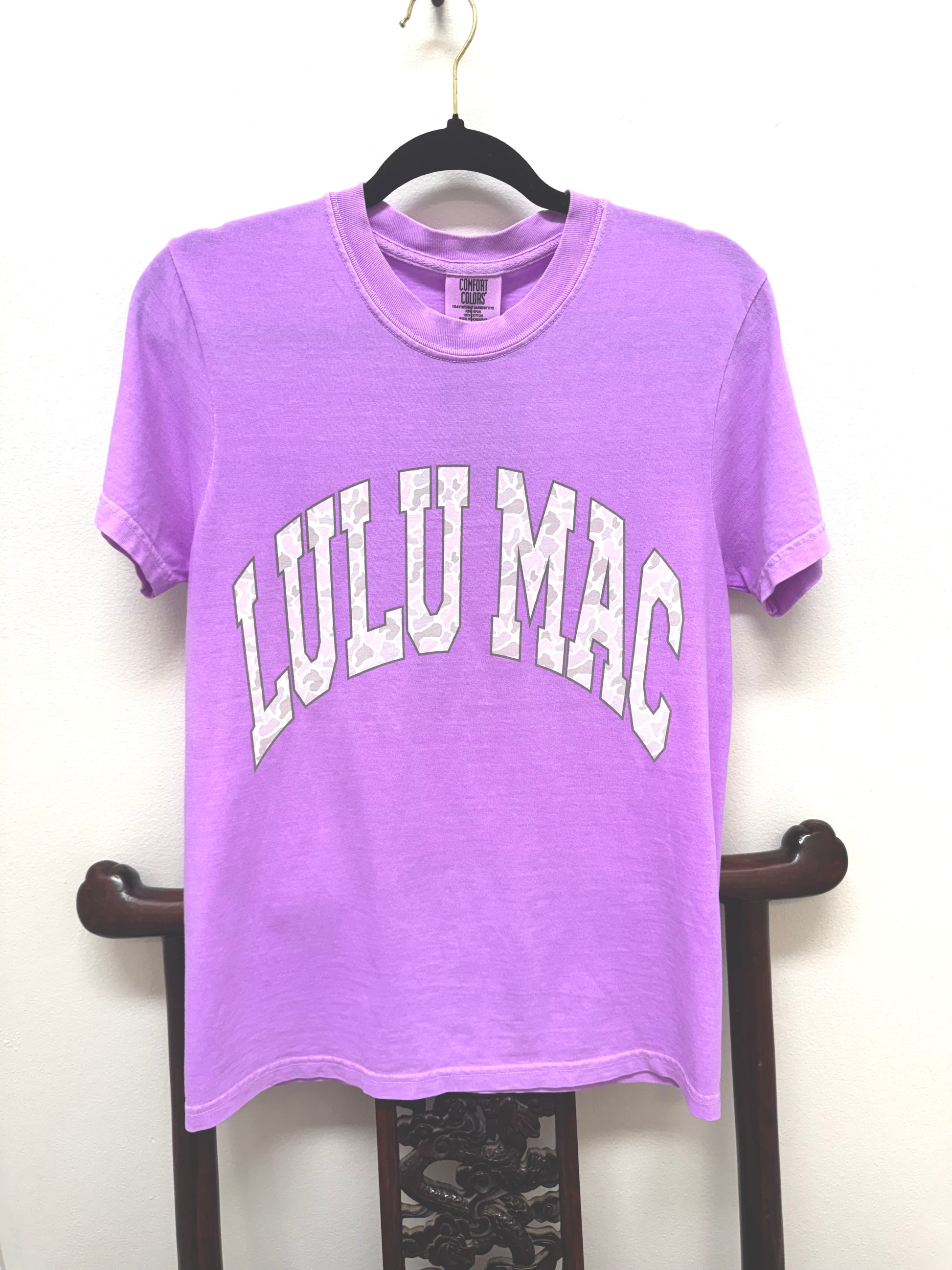 Purple t-shirt with 'LULU MAC' text on a hanger against a white background
