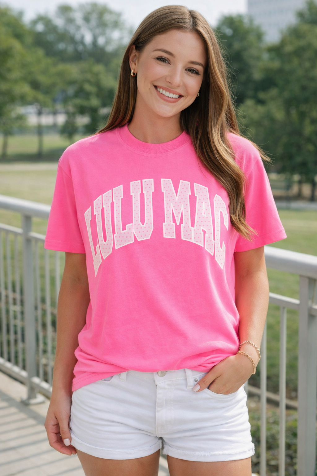 Woman wearing a bright pink t-shirt with 'Lulu Mac ' text, standing outdoors.